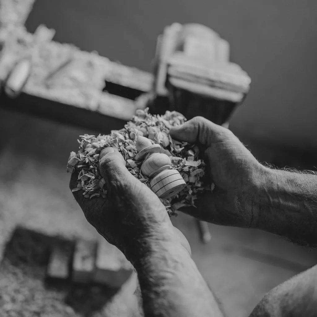 Mains d’artisan tenant une pièce tout juste tournée, au milieu des copeaux de bois