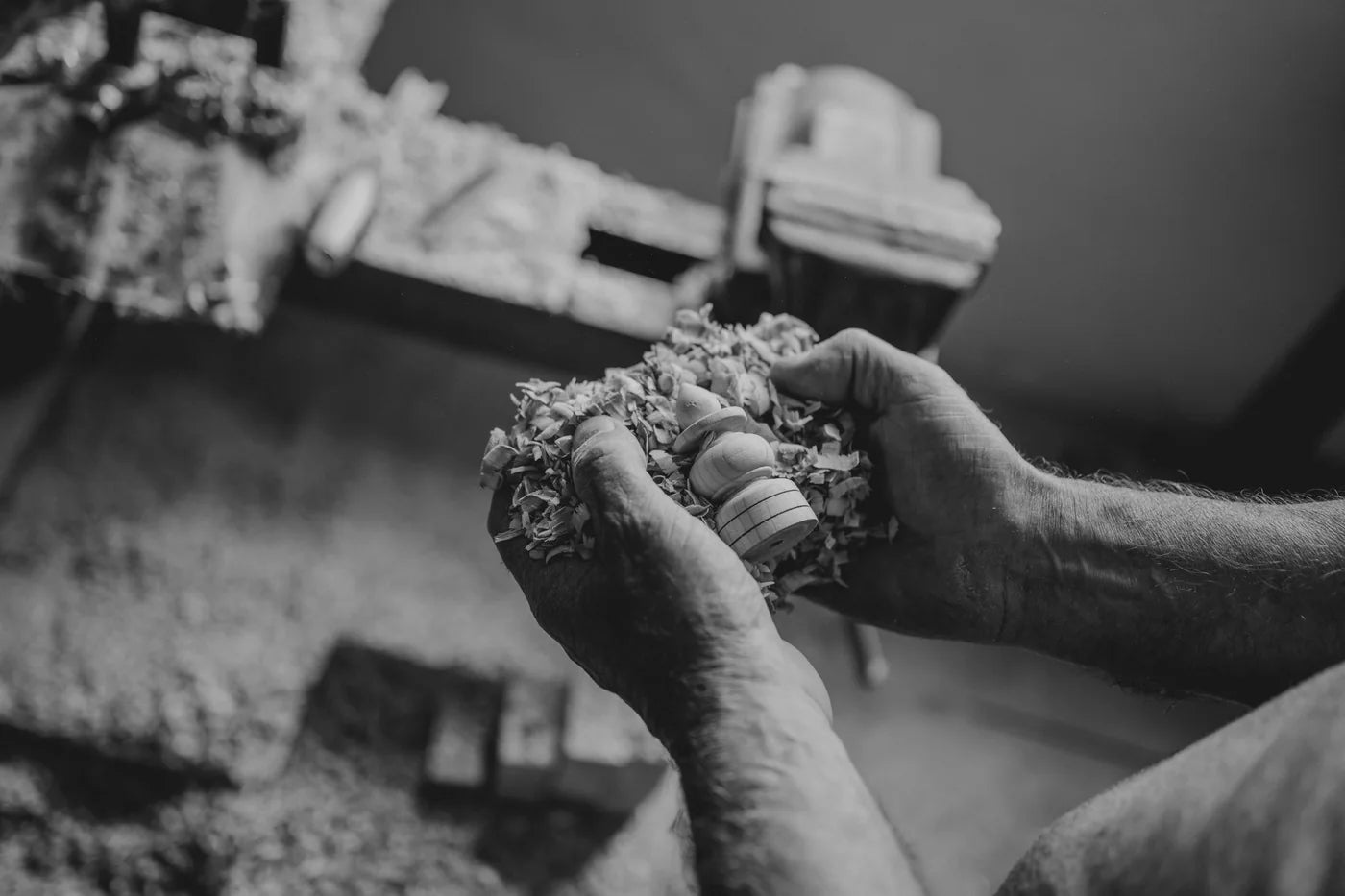 Mains d’artisan tenant une pièce au milieu des copeaux, en noir et blanc